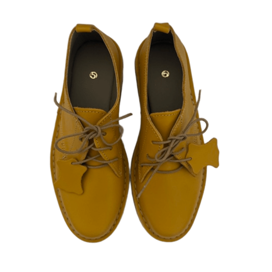 Pair of mustard yellow shoes with laces on a white background from above