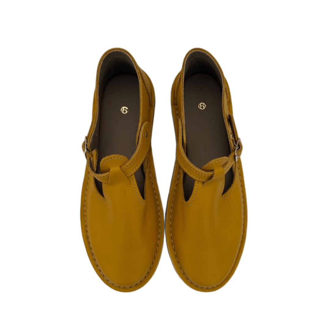 Pair of mustard yellow shoes with a buckle strap on a white background from above